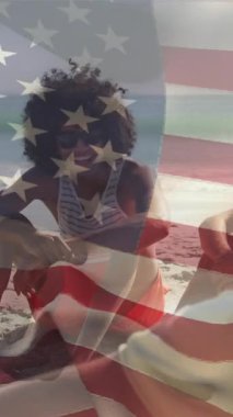 Amerika 'nın ulusal bayrağının sahilde oturan ve konuşan farklı arkadaşlar üzerindeki animasyonu. Dijital bileşim, çoklu pozlama, arkadaşlık, birliktelik, özgürlük, hükümet ve vatanseverlik kavramı.