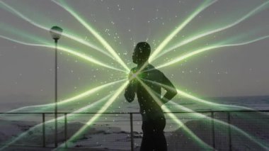 Alacakaranlıkta sahil şeridinde koşan bir adam fitness teknolojisi için göğsünü titreten yeşil enerji kanatlarını çalıştırıyor. Fitness, technology, viviviality, siluet, movement, energy, athletic