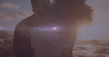 Kadın partnerine yaklaşıyor ve gün batımında Rocky Plajı 'nda sarılıyor. Yolculuğu mercekle kutluyor. Romantizm, samimiyet, günbatımı, kıyı şeridi, doğa, bağlantı, siluetler