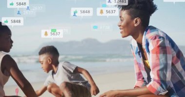 Sosyal medya simgeleri yüzerken çocuklara kumsalda kum kepçelerken anne rehberlik ediyor. Aile, açık hava, neşeli, güneş ışığı, canlı, bağlantı, boş zaman