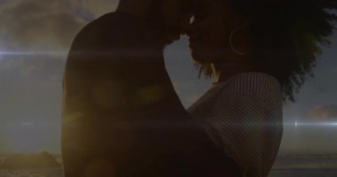 Günbatımı sahilinde kadına doğru eğilen erkek, alnı birbirine değen çift, alevler içinde dans ediyor. Romantizm, samimiyet, siluet, sahil, dinginlik, bağlantı, sıcaklık