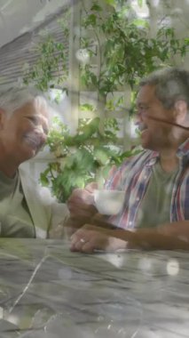 Bahçede, yaşlı bir çift kahve içiyor ve gün ışığında animasyonla sohbet ediyor. Yaşlılar, sohbet, rahatlama, arkadaşlık, sabah, doğa