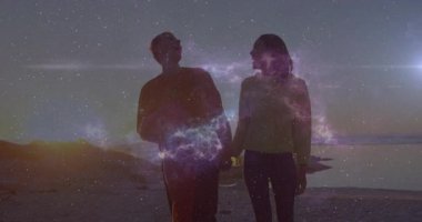 Film çifti plajda yürürken merkezde parıldayan nebula ışıklarının arkadan yandığını görür. Romantik, siluet, göksel, atmosferik, dingin, uyum, macera