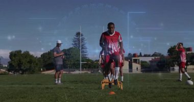 Spor koçu zamanlayıcı futbolcu engelli tatbikatı. Yüksek diz sekmelerini karıştırıyor. Turuncu engelleri aşıyor. Atletizm, eğitim, motivasyon, takım çalışması, fitness, açık hava, dinamik