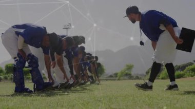 Koç çömelmiş beyzbol takımına yaklaşıyor, tatbikat için işaret veren pozisyonlarda parlayan düğümler yerleştiriyor. Atletizm, antrenman, takım çalışması, spor, performans, motivasyon, taktik