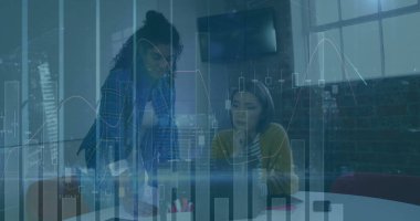 Collaborating women in business attire analyzing charts at loft office table, with laptop and mug. Collaboration, teamwork, data, analytics, corporate, professional, modern