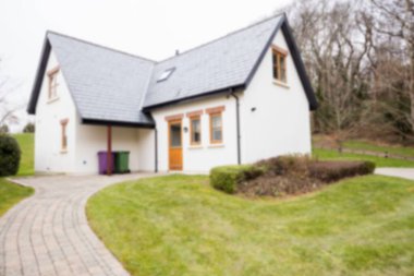 White cottage is standing on brick walkway in flat design with slate roof and colored bins. Rustic, rural, architecture, landscape, cozy, pastoral, outdoor