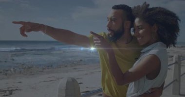 Sahildeki korkuluklara yaslanan ve ufku gezmek ve manzarayı paylaşmak için işaret eden bir adam. Romantizm, eğlence, açık hava, dinginlik, arkadaşlık, mutluluk, yaşam tarzı