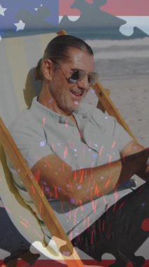 Sahilde güverte sandalyesinde oturan dijital tablet kullanan bir adama karşı Amerikan bayrağı üzerinde yapboz. Amerika 'nın bağımsızlığı vatansever tatil konsepti