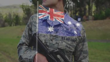 Askeriyede tüfeği tutan asker dik dik bakıyor ve şeffaf Avustralya bayrağının haraç kesmesine neden oluyor. Ordu, disiplin, vatanseverlik, yansıma, açık hava, kamuflaj, ciddiyet