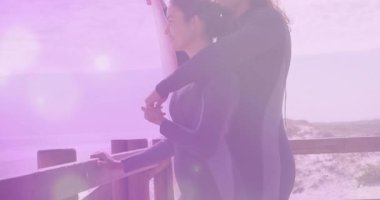 Erkek, bir sonraki dalgaya hazırlanmak için mercekli sörf tahtasında kadın ellerine rehberlik ediyor. Macera, takım çalışması, arkadaşlık, kıyı şeridi, açık hava, eğlence, canlı