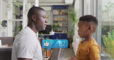 Baba diz çökmüş konuşuyor ikon gibi süzülüyor ve oğlu kucaklaşırken teknolojiyi gösteriyor. Aile, bağ, şefkat, dijital, takdir, modern, samimiyet