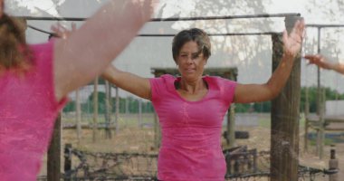 Pembe giysili bir kadın parkta demir parmaklıkların altında iple, tahta direklerle kollarını kaldırıyor. Atletik, güçlendirme, kararlılık, dayanıklılık, fitness, açık hava, toplum