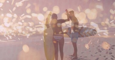 Günbatımı plajında mayo giyen sörfçü beşlik çakıyor, kumdaki ayak izleriyle. Tatil, macera, kıyı şeridi, dinginlik, eğlence, coşku, dostluk.