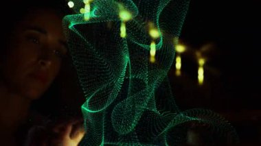 Cam panele doğru parmağını kaldıran bir kadın, teknolojik gösteride yeşil holografik ağların şekillenmesine neden oluyor. Holografi, etkileşim, dijital sanat, fütüristik, yenilik, görselleştirme, bilim