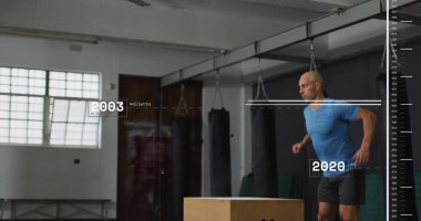 Spor kıyafetleri içinde atlayan erkek, spor salonunda plüyometrik kutu atlayışı yapıyor, kum torbalarıyla, fotokopi çekerek. Sporcu, fitness, yüksek yoğunluk, güç, güç, antrenman, egzersiz