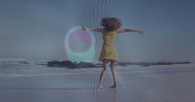 Kıyı şeridindeki ıslak kumda dans eden sarı elbiseli, dönen kadın, koyu kaya oluşumlarıyla. Özgürlük, rahatlık, kaygısız, açık hava, doğal, canlı, hareketli