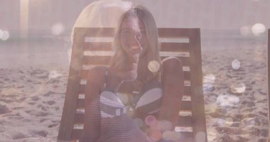 Plajdaki şezlongda bikini giyen, mercek alevleri ve sakin okyanus ufkuyla oturan kadın. Sahil, dinlenme, huzur, güneş ışığı, yansıma, tatil, yaşam tarzı.