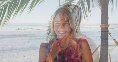 Sahilde kırmızı kareli tepesinde palmiye ağacı, hamak ve okyanus dalgalarıyla gülümseyen bir kadın. Yaz mevsimi, dinlenme, cennet, tatil, tropikal, boş zaman, huzur