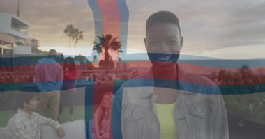 Gün batımında derinleşen adam arkadaşlarıyla sohbet ederken pazarlama için kameraları selamlıyor. Açık havada yaşam, sosyal toplantı, gün batımı manzarası, şehir çatısı, günlük yaşam tarzı, eğlence aktiviteleri, canlı renkler