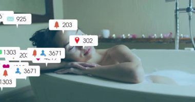 Küvete yaslanmış bir kadın çan uyarısı alıyor sonra da teknik ikonların taştığını ve dağıldığını gösteriyor. Rahatlama, sağIık, dinginlik, modern, spa, kişisel bakım, dijital aşırı yüklenme