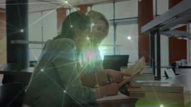 Eğitim laboratuarında parıldayan dijital örtüler ders kitabı üzerinde işbirliği yapan iki kadını kabul ediyor. İşbirliği, akıl hocalığı, meslek, öğrenme, teknoloji, çalışma alanı, iletişim