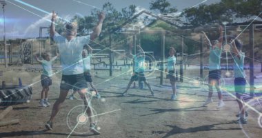 Önde gelen eğitmen ve altı çocuk toprak alanda yıldız sıçrayışları yapıyor, ahşap kirişlerle ağ hatlarıyla. Etkin açık hava, fitness, takım çalışması, gençlik sporları, oyun alanı, dijital bağlantı, fiziksel aktivite