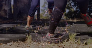 Tozluklu ve spor ayakkabılı sporcular dışarıda lastik desenli, dijital kaplamalı tatbikat yapıyorlar. Fitness, çeviklik, hareket, performans, spor, açık hava, teknoloji