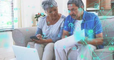 Üst düzey çift belgeleri inceliyor, dizüstü bilgisayarda geziniyor ve teknoloji ağıyla akıllı telefonları dinliyor. Nesiller, teknoloji, bağlantı, işbirliği, dijital, yaşam tarzı, ikamet