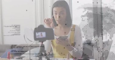 Kadın tasarımcı telefona göz ucuyla bakıyor sonra da dijital kaplamalı makyaj dersinde göz farı uyguluyor. Güzellik, kozmetik, ışıltı, etkileyici, dijital, öğretici, canlı