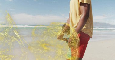 Yürüyen baba ve oğul mayo içinde kumsalda el ele tutuşuyorlar. Dalgalar, sarı parıltılar, fotokopi alanı. Aile, bağ, eğlence, canlı, açık hava, sükunet, kutlama