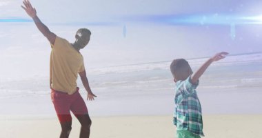 Sarı gömlekli bir baba ve kumlu sahilde yeşil ekose gömlekli bir oğul, dalgalar havada uçuşuyor. Aile, açık hava, rahatlama, oyun, neşe, ufuk.