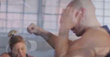 Stüdyoda ortaklarla boks antrenmanı yapan üstsüz bir adamı yumruklamak. Şebeke camları, beyaz kulaklıklar. Spor, spor, atletik, kardiyo, yoğunluk