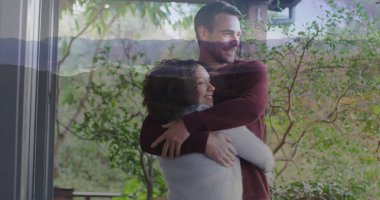 Verandada örgü süveter giyen, cam kapı çerçevesi ve güverte korkuluklarıyla sarılan çift. Romantik, sevecen, rahat, sakin, kırsal, yeşillik, açık hava