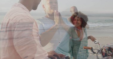 Sahilde dalgalı yeşil elbise ve pembe gömlek giyen, bisikletli ve dalgalı duran çiftler. Romantizm, eğlence, sükunet, tatil, yaşam tarzı, uyum, doğal