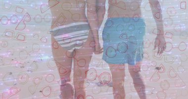 Sahil şeridi boyunca el ele tutuşan yürüyen çift, çizgili bikini tabanı ve deniz mavisi mayolarıyla. Aşk, eğlence, yaz, açık hava, dinginlik, yaşam tarzı, moda.