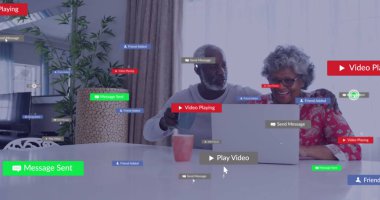 Ev oturma odasındaki masada yüzen ikonlarla kahve fincanı tutan dizüstü bilgisayarlı yaşlı çift görülüyor. Kentsel, modern, rahat, teknoloji, samimiyet, yaşam tarzı, bağlantı