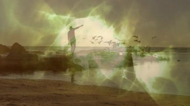 Gün batımında kayalık sahilden gelen deniz kuşlarına el kol hareketi yapan bir adam teknolojiyi gösteriyor. Macera, keşif, doğa, sükunet, ufuk, ilham, vahşi doğa.