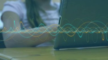 Öğrenci tablet ekranını tıklatıyor ve masada öğrenirken canlı ses dalgalarının titremesine neden oluyor. Teknoloji, eğitim, dokunmatik ekran, yenilikçi, yaratıcılık, konsantrasyon, dijital