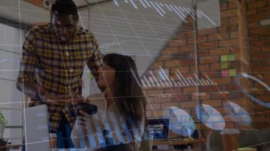 Adam, VR kulaklık kontrollerini ayarlayan kadına rehberlik ederken teknik veri tabloları güncelleniyor. Teknoloji, yenilik, işbirliği, veri analizi, dalgın, dijital, analitik