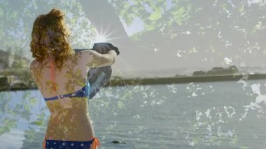 Mavi mayo giymiş bir kadın havluyu kavrayıp göl kenarında yüzdükten sonra belini sarmak için açıyor. Yaz zamanı, boş zaman, rahatlama, açık hava, doğal, manzaralı, yaşam tarzı