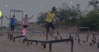 Sarı tişörtlü dengeli bir kadın park fitness alanında tahta kirişleri aşıyor, destek direkleriyle. Atletik, açık hava, egzersiz, takım çalışması, sağlık, kırsal, aktif giysi