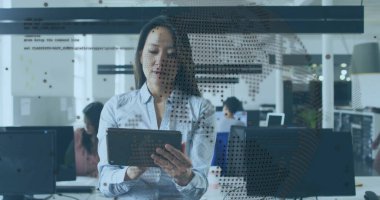 Ayakta duran Asyalı proje yöneticisi tableti açık planlama ofisinde tutuyor, dünya haritası ve kod örtüsüyle birlikte. İşbirliği, teknoloji, takım çalışması, modern, profesyonel, veri, analiz