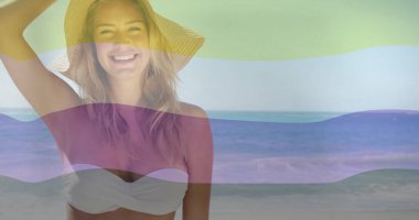 Saman güneş şapkası takan gülümseyen kadın ve beyaz askısız mayo kıyıda duruyor, renkli bantlar. Plaj, boş zaman, yaz, açık hava, sükunet, moda, rahatlama