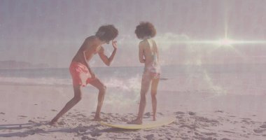 Güneşli sahil şeridinde, yumuşak okyanus dalgalarıyla sarı sörf tahtasında duran dengeli arkadaşlar. Sahil şeridi, boş zaman, yaz, macera, minimalist, arkadaşlık, açık hava