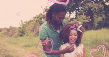 Küçük bir nesne tutuyor, çim tarlasında ağaçların yanında duran, şeffaf kalp grafikleriyle. Romantik, aşk, doğa, bağlantı, dinginlik, sıcaklık, organik