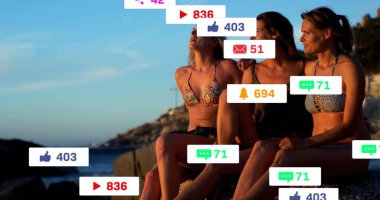 Bikinili üç arkadaş kayalık sahilde yüzen sosyal medya simgeleriyle gün batımını izliyorlar. Sahil, gün batımı, arkadaşlık, rahatlama, deniz kenarı, hayat dolu.