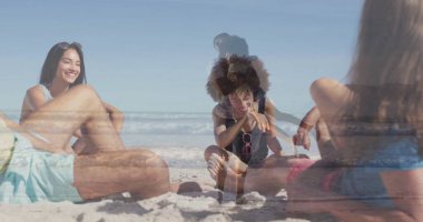 Pembe güneş gözlükleri ve plaj havlusuyla kumlu sahil şeridinde oturan bir grup yetişkin ve kız. Aile, eğlence, yaz, açık hava, eğlence, mutluluk, birliktelik.