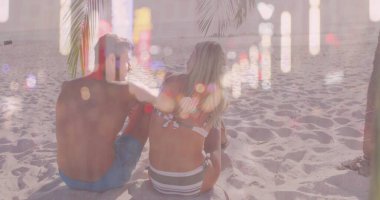 Okyanus ufkuna bakan, mayo giyen çift güneş ışığında kumsalda palmiye yapraklarının altında oturuyor. Rahatlama, tropikal, rahatlık, romantizm, dinginlik, doğa, manzara