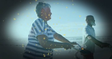 İki bisikletli, temiz gökyüzünün altında kumlu okyanus kıyısında pedal çeviren olgun bir çift. Macera, boş zaman, açık hava, refah, sahil manzarası, aktif